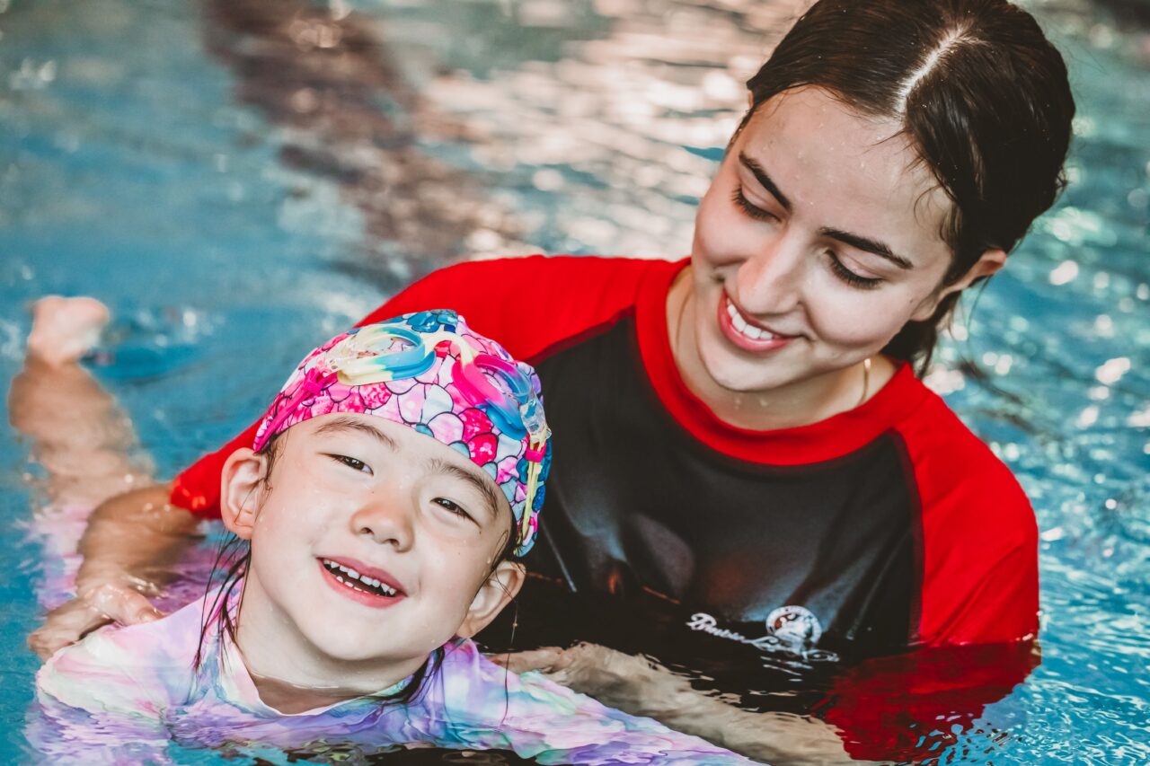 Pymble Swimming instructor smiling with a young student wearing a swim cap and goggles