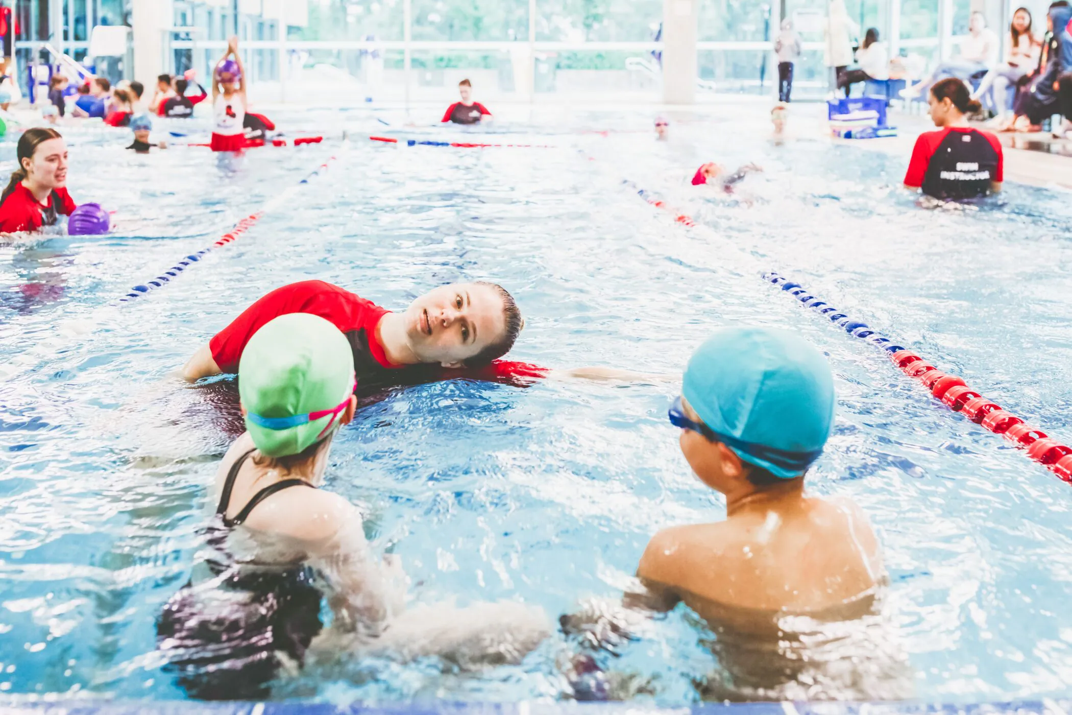 Pymble Swimming instructor talking with two students during a busy group lesson