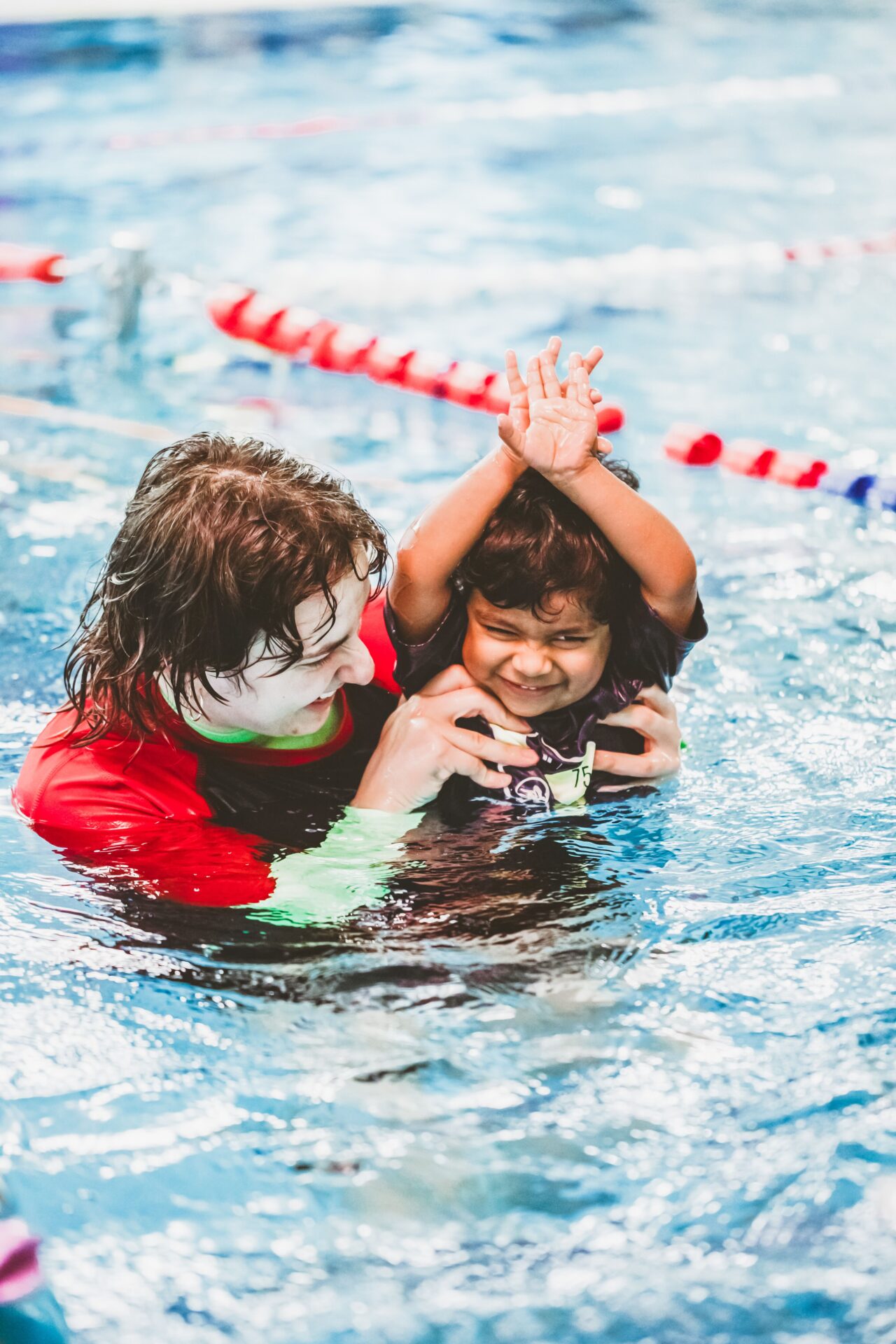 Pymble Swimming instructor playing with a toddler, arms raised above the water
