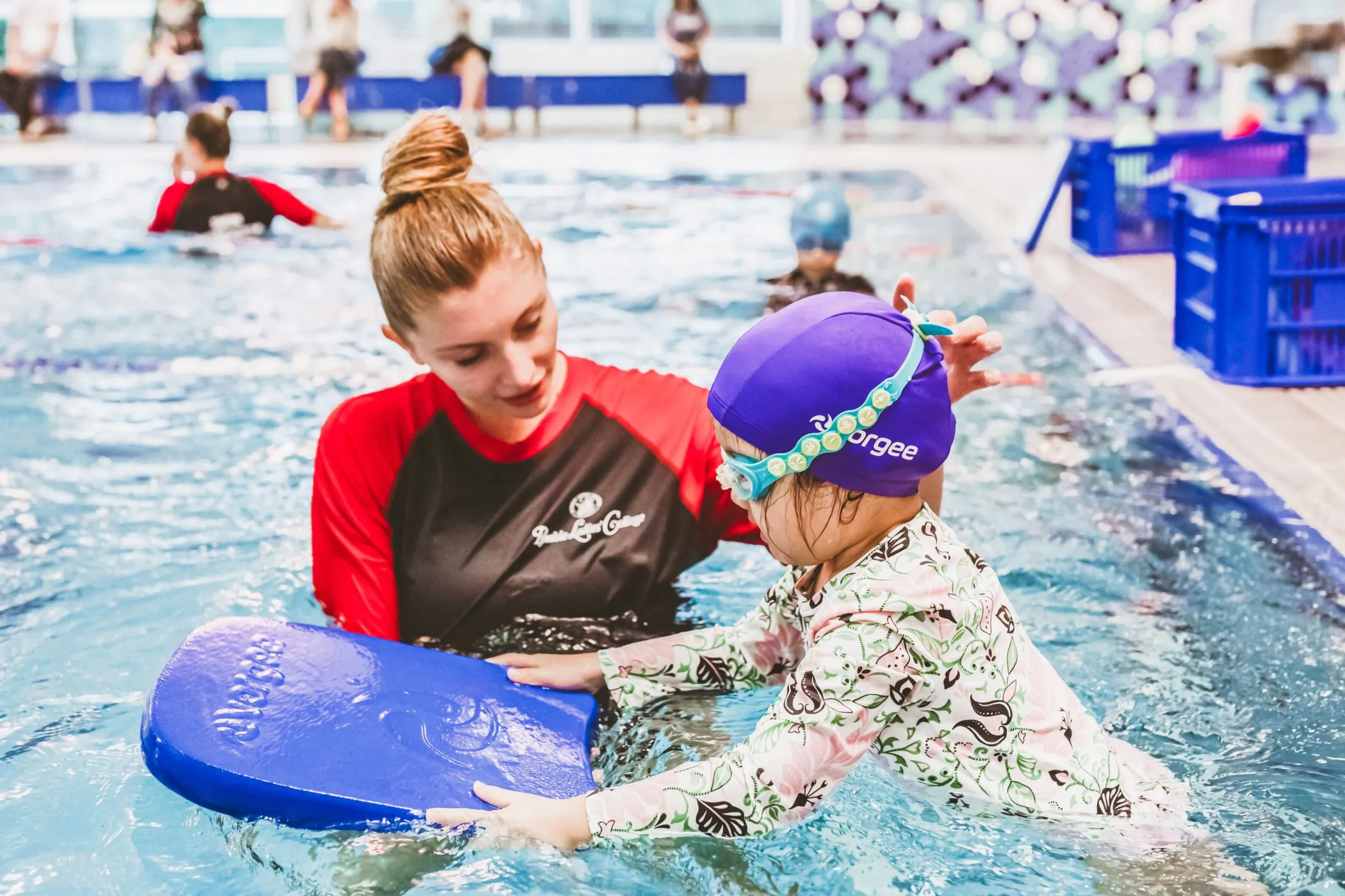 Pymble Swimming instructor helping a toddler hold a kickboard in the pool